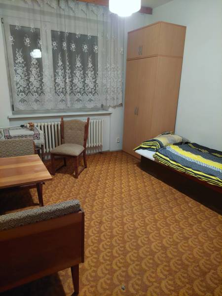 A room in a family house with a bed, wardrobe, table, and chairs, decorated in warm colors.