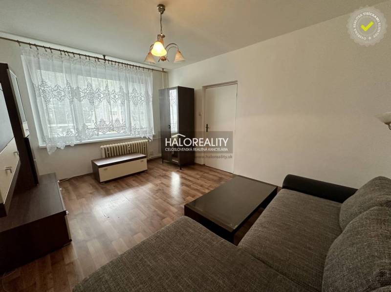 Living room in a one-room apartment with a window, curtains, dark furniture, and a sofa.
