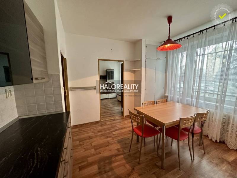 Dining room in a one-bedroom apartment with wooden floors and a large window with lace curtains.