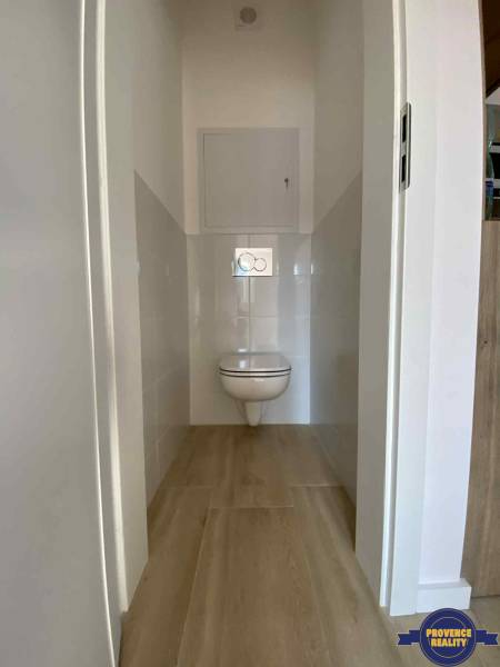 A toilet with a wall-hung WC and tiling in a 3-room apartment, with wooden flooring.