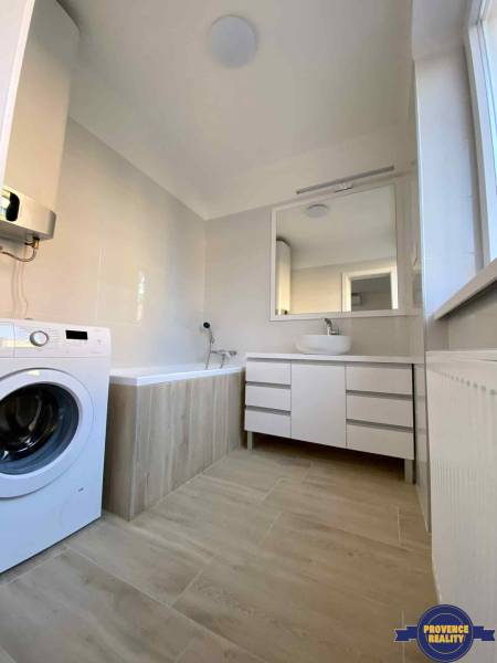A bathroom in a 3-room apartment with a bathtub, a washing machine, and a cabinet under the sink.