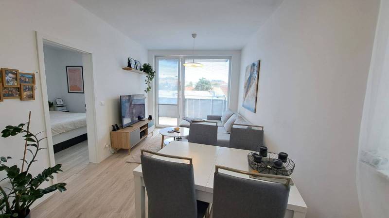 A bright living room with white furniture and an entrance to the bedroom in a two-room apartment.