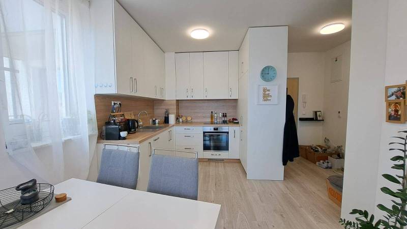 A kitchen in a 2-room apartment with a white kitchenette, dining table, and wooden floor.
