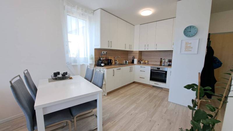 A kitchen in a 2-room apartment with a white kitchen unit, a dining table, and wooden flooring.