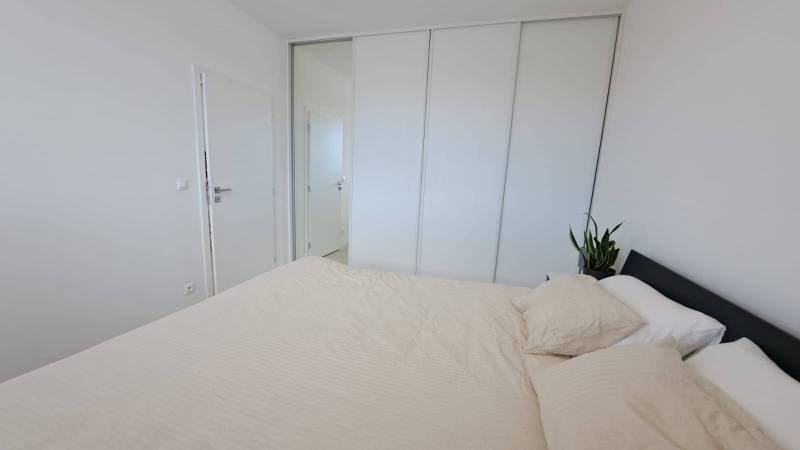 Bedroom with a bed and a built-in wardrobe in a 2-room apartment, with a plant on the nightstand.