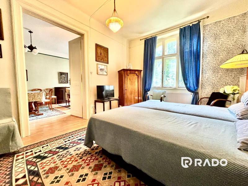 A bedroom in a 2-room apartment with a bed, blue curtains, and an oriental rug.