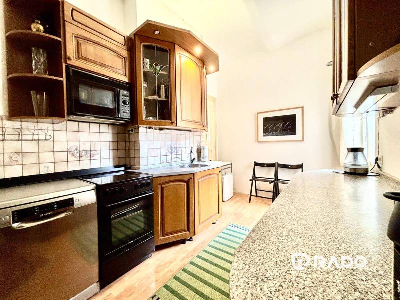 A kitchen in a 2-room apartment with wooden furniture, a stove, a microwave, and a dishwasher.