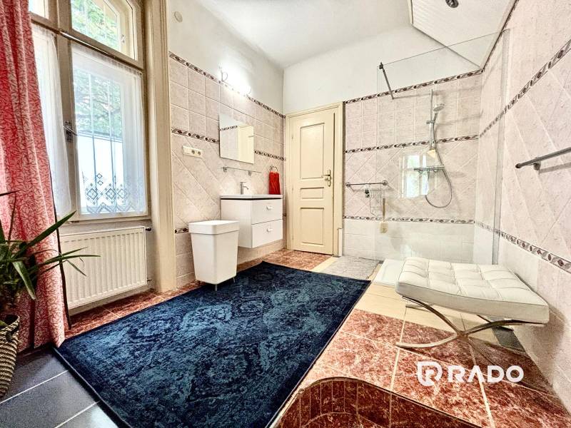 A bathroom in a 2-room apartment with a window, a bathtub, and a blue carpet.