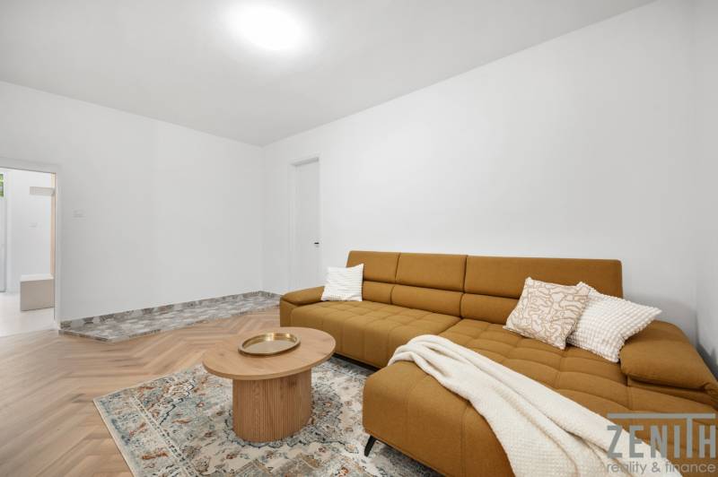 A room in a 3-room apartment with a brown sofa, a table, and a patterned carpet.