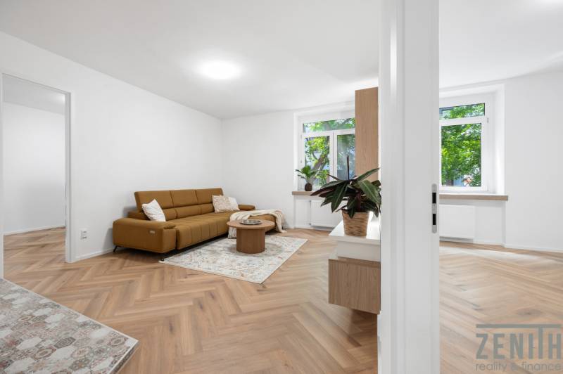 Living room in a three-room apartment with a brown sofa and wooden floor.