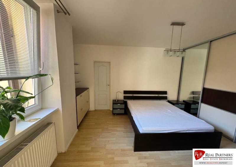 Bedroom in a 2-room apartment with a bed, wardrobe, and a large window with a flower.