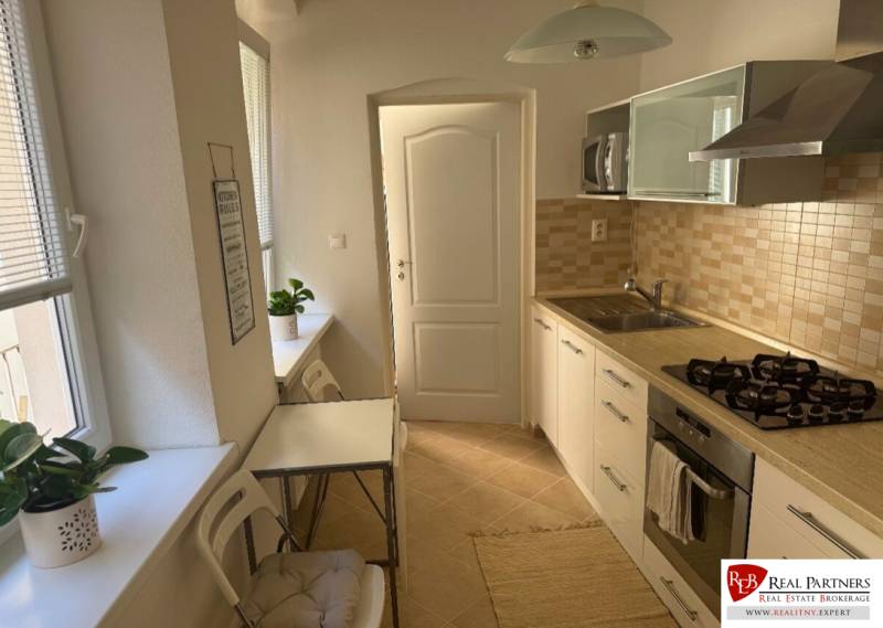 A kitchen in a 2-room apartment with light furniture, appliances, and a dining table.