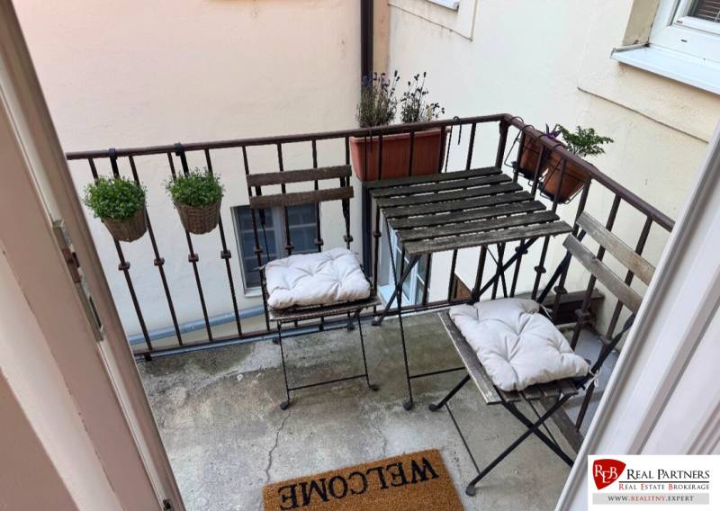 A balcony of a 2-room apartment with metal furniture and flower pots.