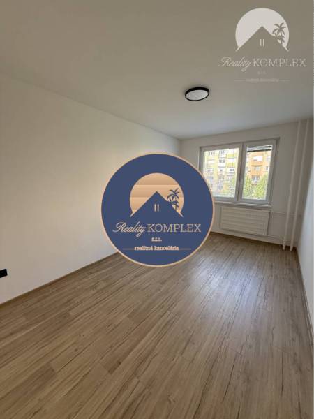 An empty room with a wooden floor in a 3-room apartment, a large window and a radiator under it.