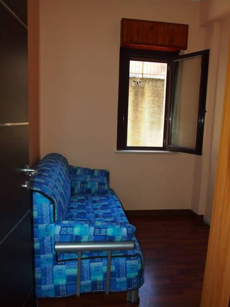 A blue sofa by an open window in a three-room apartment with wooden flooring.