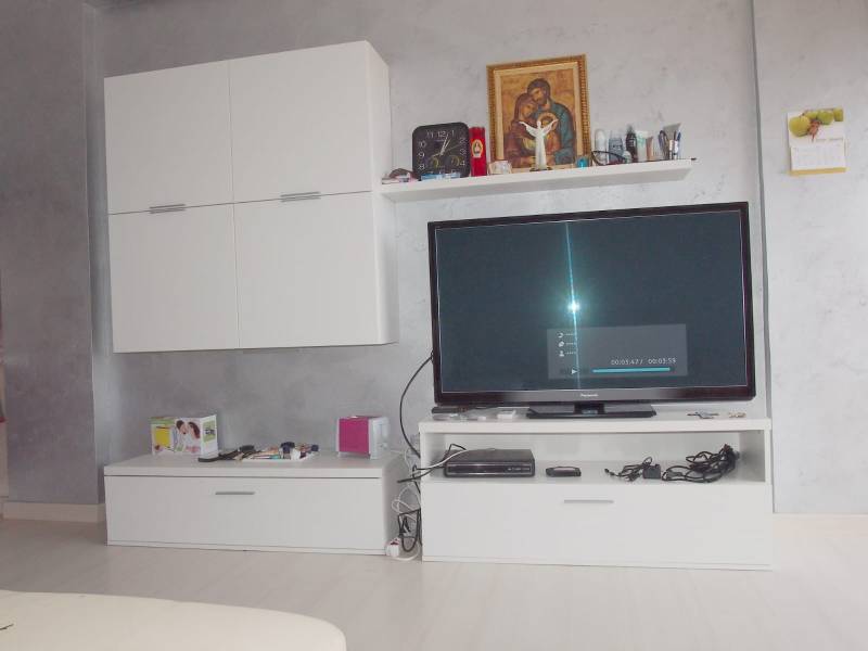 Furnishing in a 3-room apartment with white cabinets and a television on a gray painted wall.