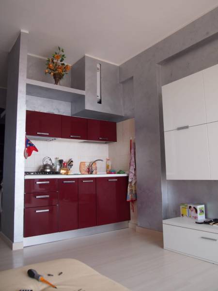 A kitchen unit in a 3-room apartment with glossy red cabinets and decoration on the shelf.