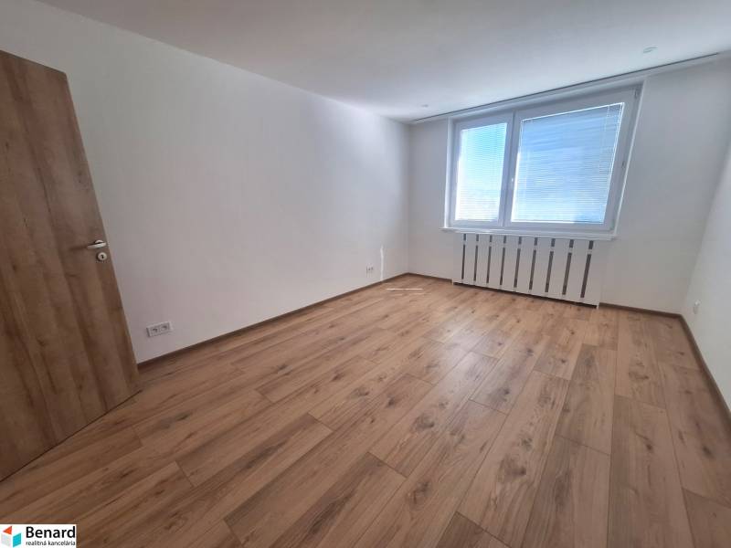 A spacious room with wooden flooring and a large window in a 2-room apartment.