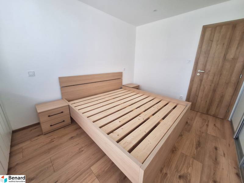 A bedroom with a wooden bed in a two-room apartment, without a mattress and with a nightstand.