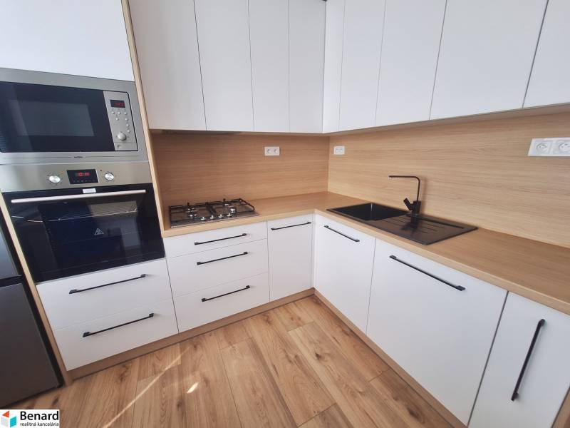 A kitchen in a 2-room apartment with wooden flooring and built-in appliances.