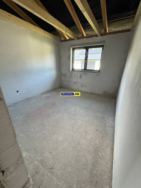 Unfinished room in a family house with a window and exposed roof beams.
