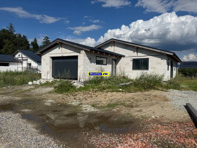 An unfinished family house in Valča with a garage, surrounded by nature and construction materials.