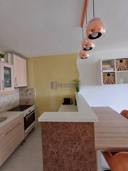 A kitchen in a 2-room apartment with soft pastel colors and pendant lights.