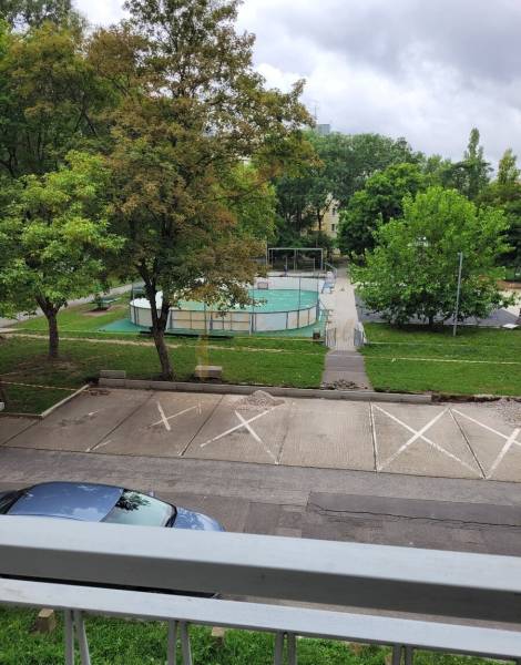 View from a 3-room apartment in Bratislava - Ružinov on Mesačná Street, parking lot, trees, and playground.