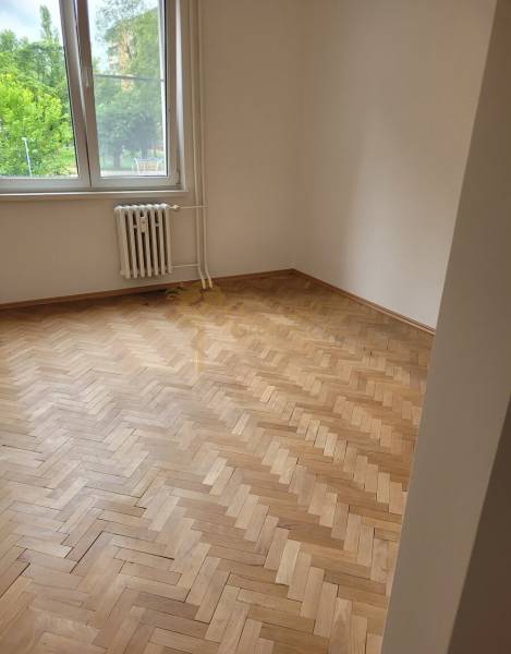 A room in a 3-room apartment with wooden parquet floors, a large window, a radiator underneath it.