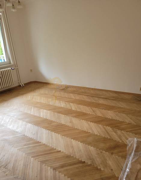 An empty room in a 3-room apartment with a parquet floor and a window.