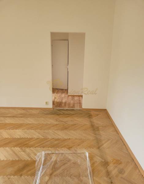 A room with a wooden floor and a white wall in a 3-room apartment.