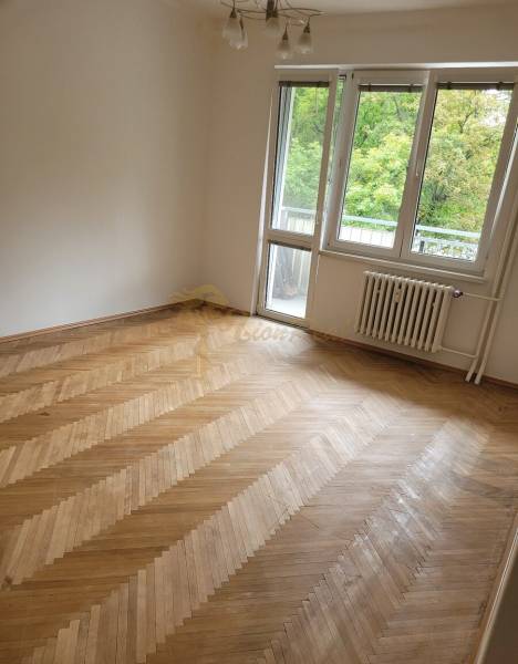 A room in a 3-room apartment with wooden flooring and balcony doors.