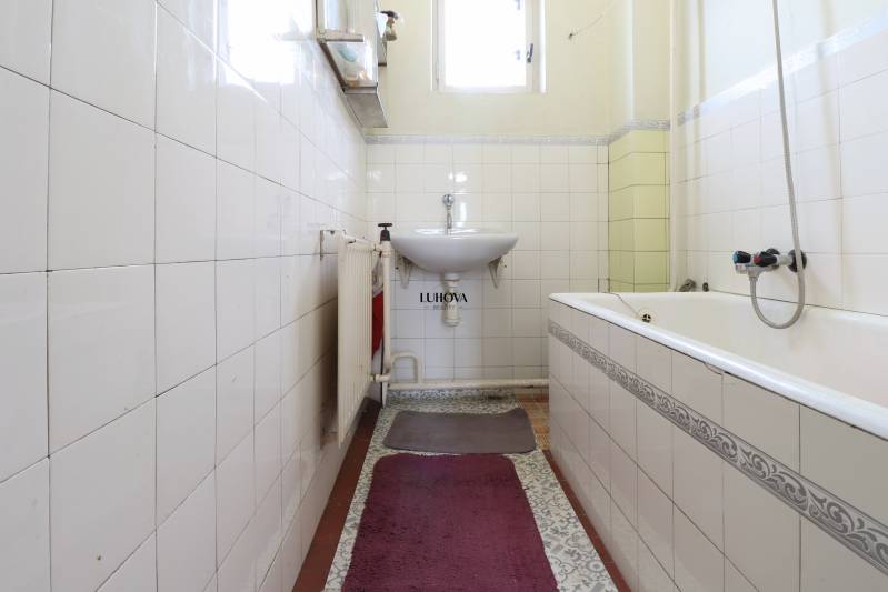 A bathroom in a family house with a bathtub, sink, and radiator. White tiles on the walls.