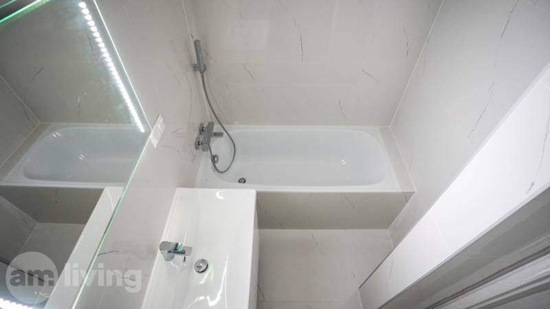 A bathroom with a bathtub, a sink, and a mirror in a 2-room apartment.