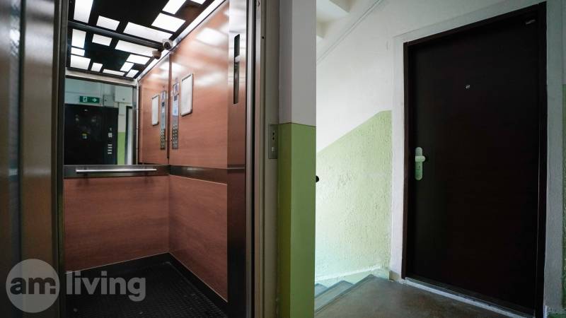 An elevator with a wooden decor and a staircase with doors to a 2-room apartment.