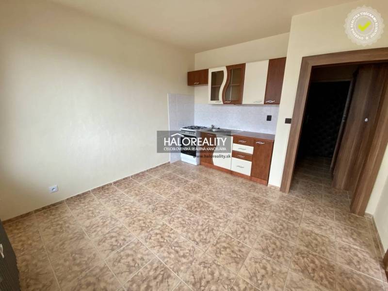 Kitchen in a studio apartment with tiled floor and cabinets.