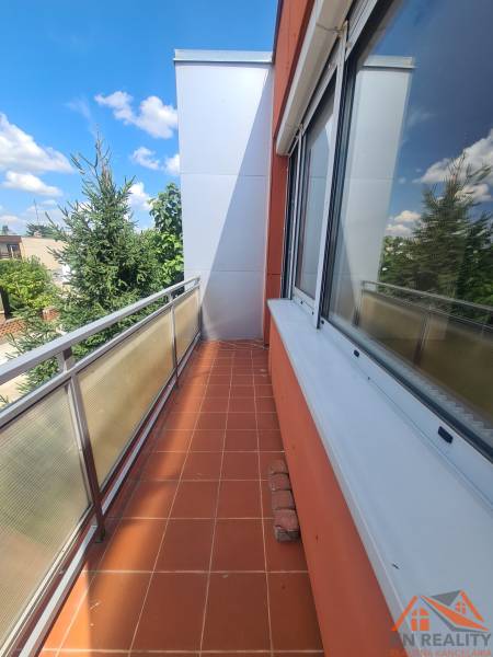 A balcony of a family house in Nové Zámky with tiles and a view of the trees.