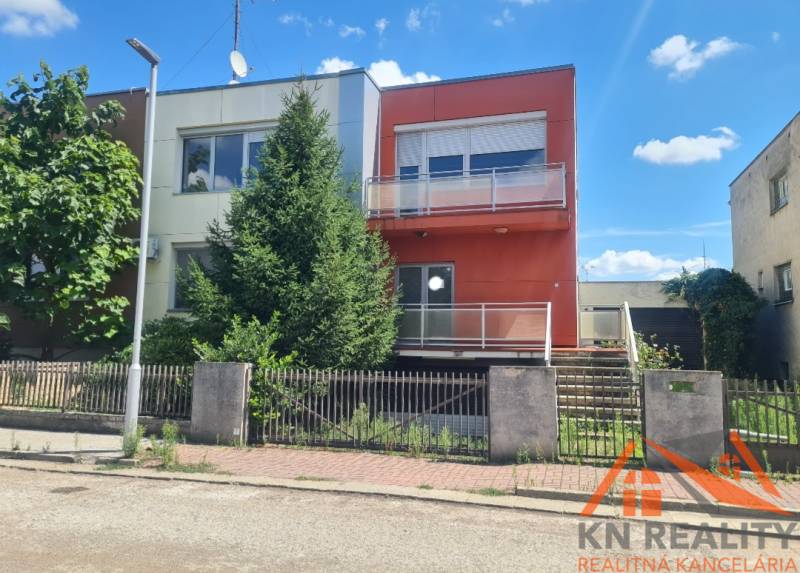 A family house in Nové Zámky with trees in front of the entrance and an orange facade.
