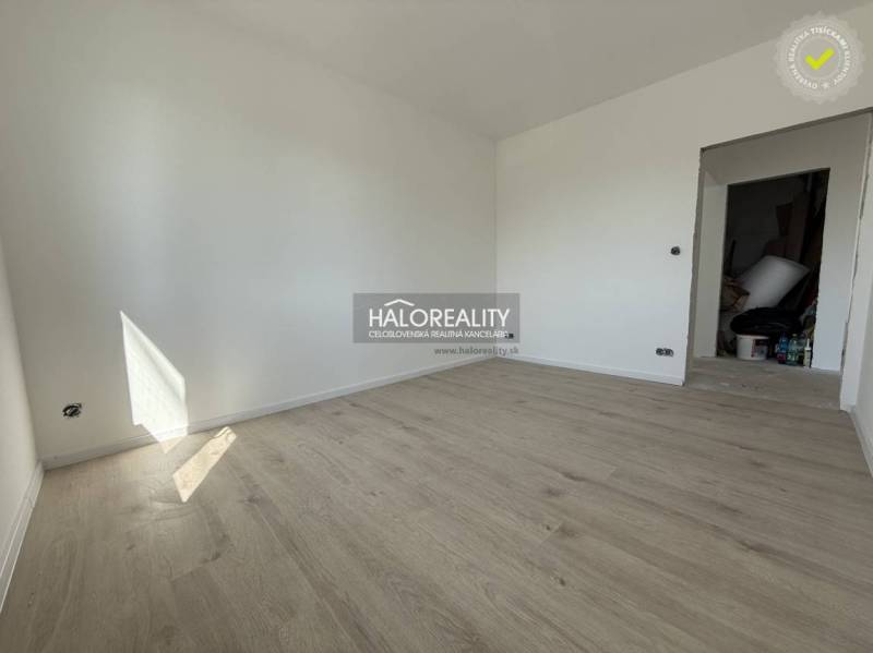 A room with a wooden floor in a family house, white walls, and open doors.