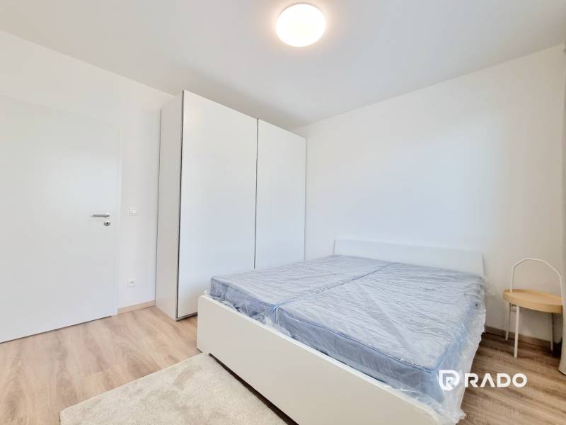 A bedroom in a 3-room apartment with a bed, a white wardrobe, and wooden flooring.