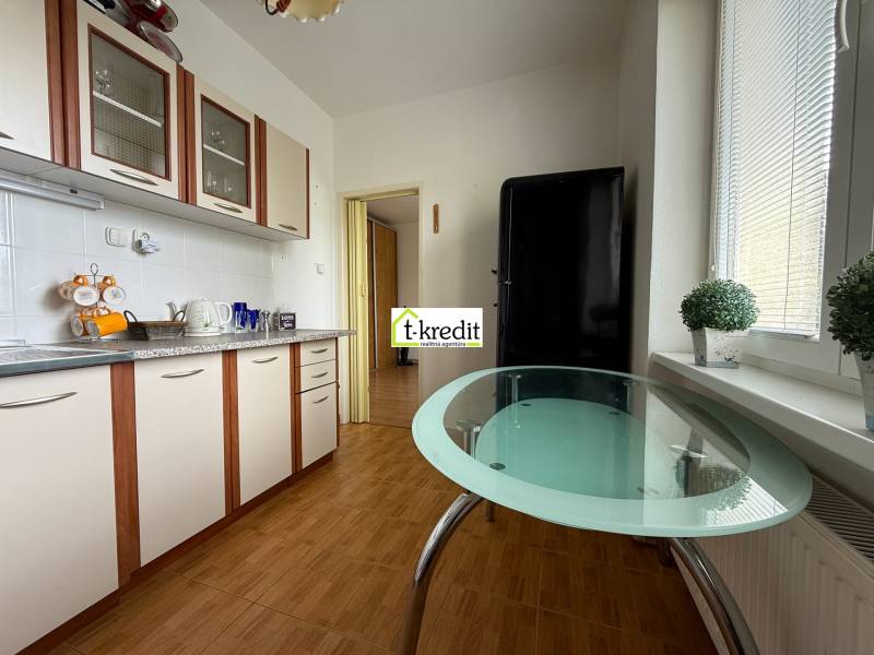 A kitchen in a 2-room apartment with a glass table and white cabinets.