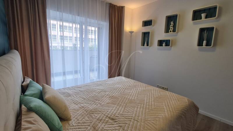 Bedroom in a two-room apartment with a bed, pillows, and decorative shelves on the wall.