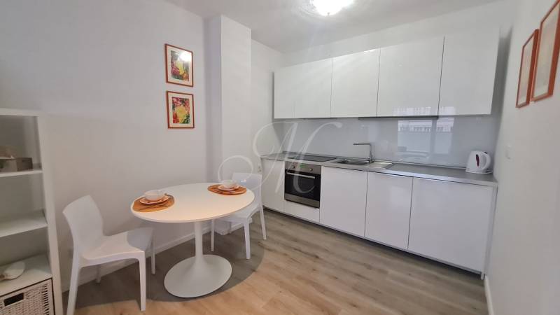 A kitchen in a 2-room apartment with white furniture, a dining table, and decorations.