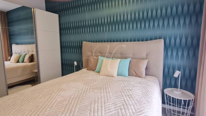 A bedroom in a two-room apartment with a bed, colorful pillows, and a textured wall.