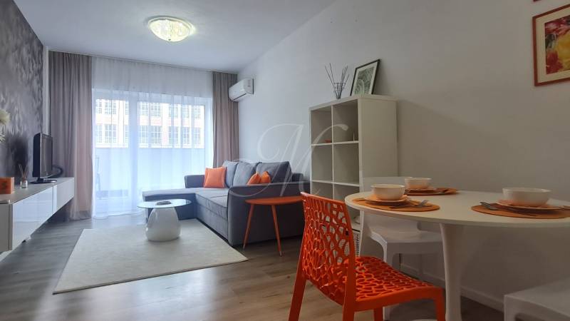 Living room in a two-room apartment with a sofa, dining table, and colorful accessories.
