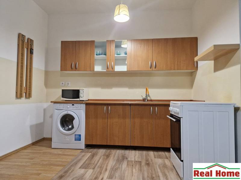 Kitchen in a studio apartment with a stove, microwave, and washing machine, wooden cabinets.