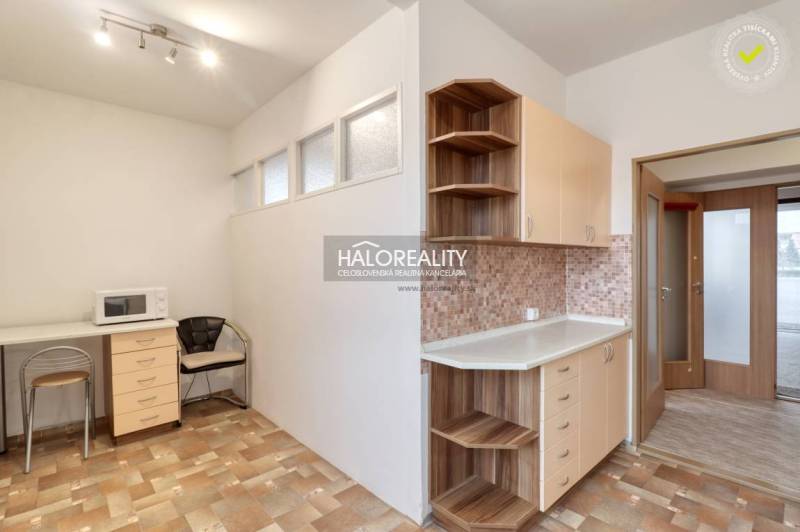 A kitchen in a 3-room apartment with a microwave, a chair, and cabinets for storage.