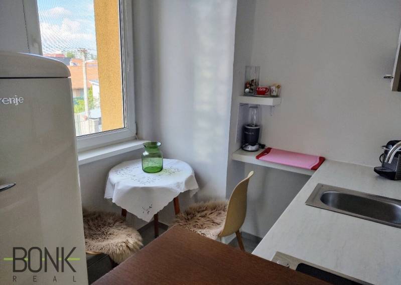 A kitchen in a 2-room apartment with a window, a bar counter, and a dining area.
