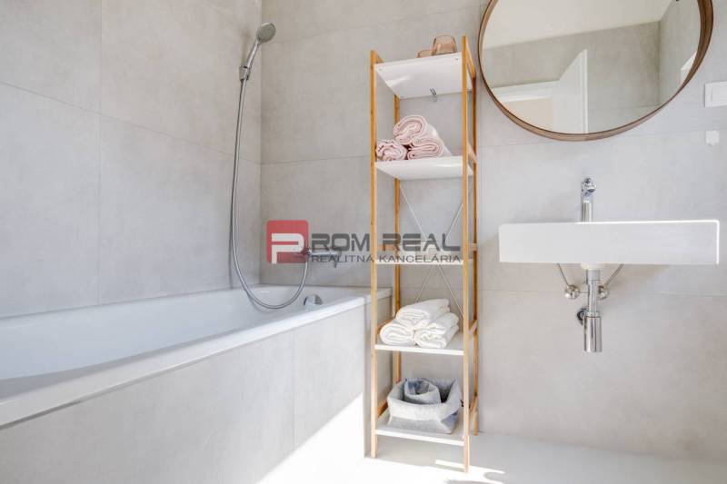 A bathroom in a 3-room apartment with a bathtub, open shelf, and mirror on the wall.