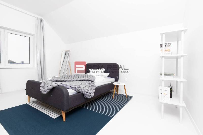 A bedroom in a 3-room apartment with a modern bed, a shelf, and white walls.